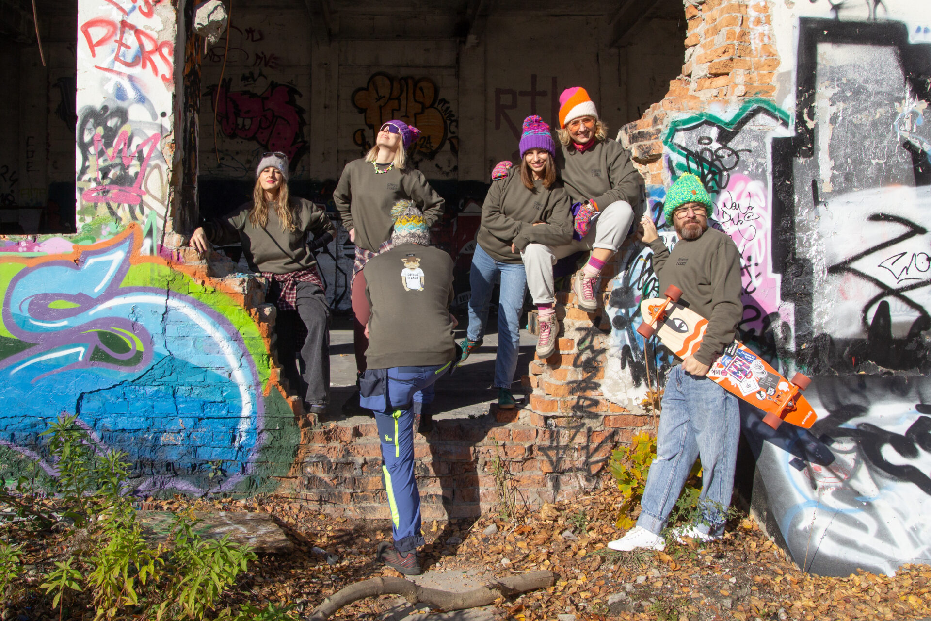 grupa ludzi stoi na tle grafitti w bluzach LaQ Dzikus z Lasu